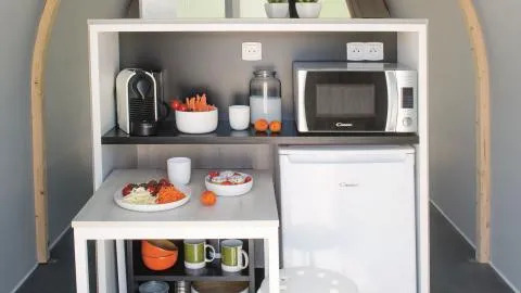 Compact keukentje in een safaritent met frigo, microgolfoven, koffiemachine en ontbijt op de tafel.