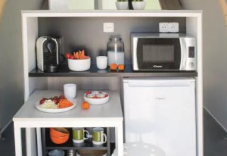 Compact keukentje in een safaritent met frigo, microgolfoven, koffiemachine en ontbijt op de tafel.