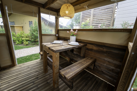 Houten tafel en banken in de Airstay safaritent aan Lago Idro Glamping Boutique, Italië, met sfeervolle lamp.