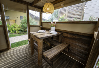 Houten tafel en banken in de Airstay safaritent aan Lago Idro Glamping Boutique, Italië, met sfeervolle lamp.