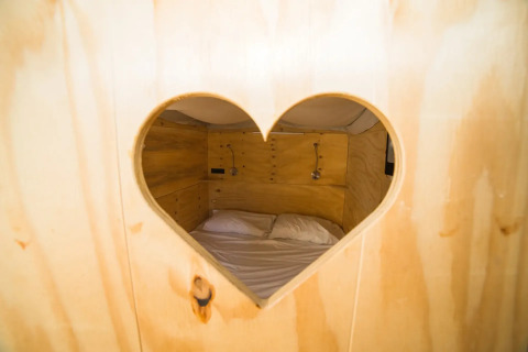 Uitzicht door een hartvormig venster op een houten slaapplek in Airlodge 2.0, Lago Idro Glamping Boutique.
