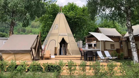 Foto di Tipi Lodge con una grande tenda tipi, terrazza, sedie, tavoli e circondata dal verde.