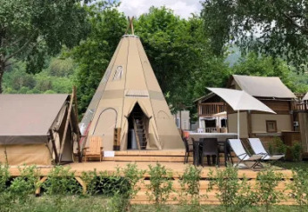 Foto de Tipi Lodge con una gran tienda tipi, terraza, sillas, mesas y vegetación verde alrededor.