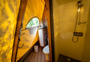 Baño moderno dentro de una tienda tipi, con iluminación amarilla, ducha, inodoro y ventana en Lago Idro Glamping Boutique.