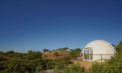 Dome House bij Wecamp Reserva Alecrim in Portugal, met een koepelwoning en heuvelachtig landschap onder blauwe lucht.