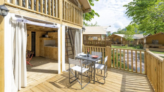 Veranda in legno del safari tent Air Lodge 2.0 con tavolo da pranzo, sedie e vista su altre tende glamping.