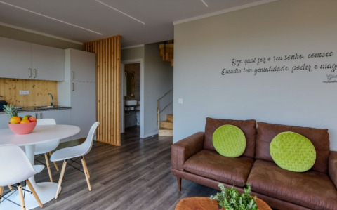 Sfeervolle zithoek met bruine sofa, groene kussens en keuken in Dome House Duplex, Wecamp Reserva Alecrim, Portugal.