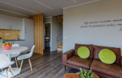 Sfeervolle zithoek met bruine sofa, groene kussens en keuken in Dome House Duplex, Wecamp Reserva Alecrim, Portugal.