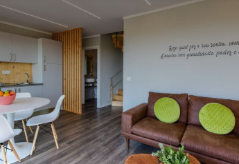 Acogedora sala con sofá marrón, cojines verdes y cocina en Dome House Duplex, Wecamp Reserva Alecrim, Portugal.