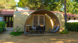 Tenda safari Coco Suite con veranda, tavolo, sedie e sdraio all’aperto, tra alberi e piante.