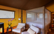 Interior de tienda safari en Lodge Family, Wecamp Reserva Alecrim en Portugal, con cama y sillones.