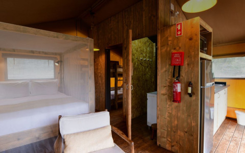 Interior de la tienda safari Lodge Family en Wecamp Reserva Alecrim, Portugal, con cama, cocina y detalles de madera.