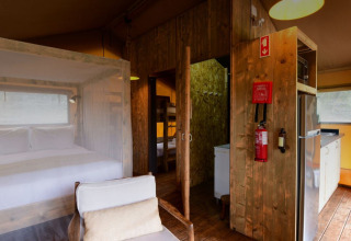 Interior de la tienda safari Lodge Family en Wecamp Reserva Alecrim, Portugal, con cama, cocina y detalles de madera.