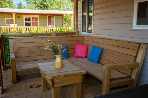 Terraza de madera con banco esquinero y cojines coloridos en un lodge, jarra amarilla con flores.