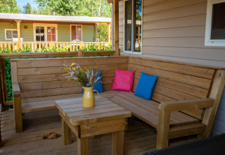 Terraza de madera con banco esquinero y cojines coloridos en un lodge, jarra amarilla con flores.