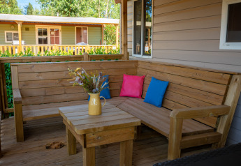 Terrasse en bois avec banc d’angle et coussins colorés dans un lodge, pichet jaune avec fleurs.