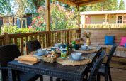 Terrazza all'aperto di un lodge con tavolo apparecchiato, ciotole, tazze, pane e verde intorno.