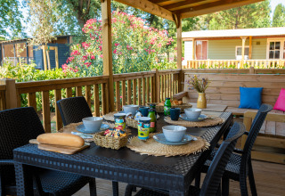 Terrasse extérieure d’un lodge avec table dressée, bols, tasses, pain et végétation autour.