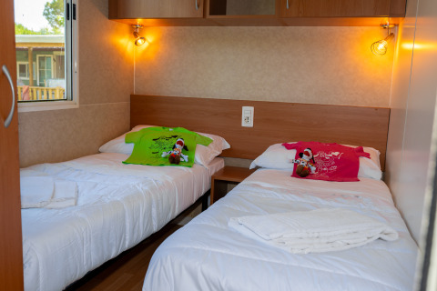 Chambre de lodge avec deux lits simples, t-shirts colorés, peluches, éclairage chaleureux et fenêtre.