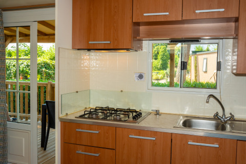 Pequeña cocina moderna en una cabaña con fogón de gas, fregadero, armarios de madera y terraza exterior.
