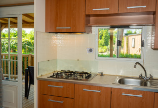 Pequeña cocina moderna en una cabaña con fogón de gas, fregadero, armarios de madera y terraza exterior.