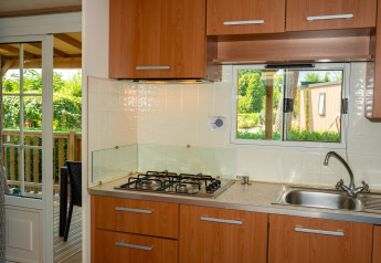 Pequeña cocina moderna en una cabaña con fogón de gas, fregadero, armarios de madera y terraza exterior.