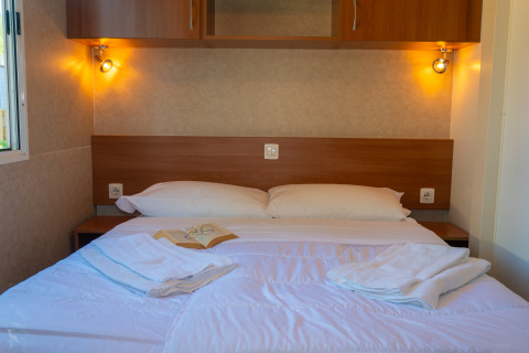 Acogedora habitación de lodge con cama doble, almohadas blancas, toallas y luz ambiental cálida.