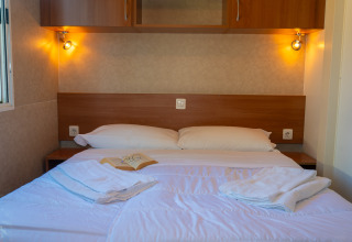 Acogedora habitación de lodge con cama doble, almohadas blancas, toallas y luz ambiental cálida.