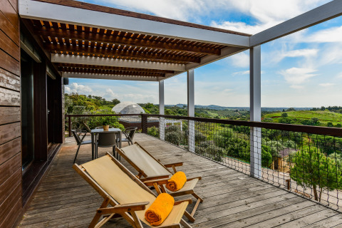Houten terras met ligstoelen en tafel, uitkijkend op groene heuvels bij Bungalow Family, Wecamp Reserva Alecrim, Portugal.