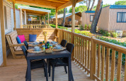 Veranda in legno al Cottage Classic del Trasimeno Glamping Resort, Italia, con tavolo apparecchiato e panca.