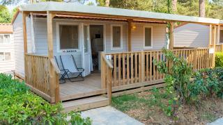 Buitenaanzicht van de Cottage Classic Midi met overdekte veranda, twee stoelen en veel groen eromheen.