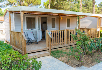 Vista exterior del lodge Cottage Classic Midi con porche cubierto de madera, dos sillas y vegetación alrededor.