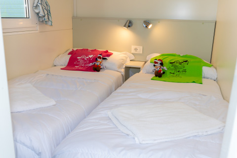 Dos camas individuales con camisetas coloridas y peluches en una habitación Cottage Classic en Trasimeno Glamping Resort.