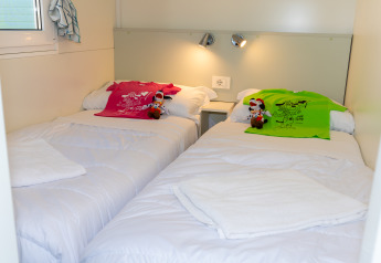Dos camas individuales con camisetas coloridas y peluches en una habitación Cottage Classic en Trasimeno Glamping Resort.
