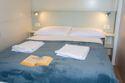 Dormitorio con cama doble, toallas blancas, libro sobre manta azul y luces de pared en Cottage Classic, Italia.
