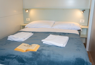 Dormitorio con cama doble, toallas blancas, libro sobre manta azul y luces de pared en Cottage Classic, Italia.