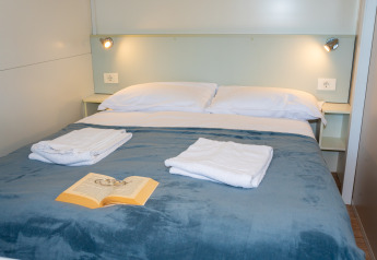 Dormitorio con cama doble, toallas blancas, libro sobre manta azul y luces de pared en Cottage Classic, Italia.