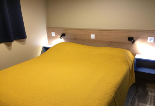 Kamer van Bungalow Family Premium, Wecamp Sao Miguel, Portugal, met dubbel bed en gele sprei.