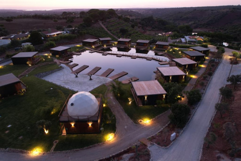 Luchtfoto van Dome House Duplex Do Lago-lodge in Wecamp Reserva Alecrim, omringd door chalets en vijver in Portugal.