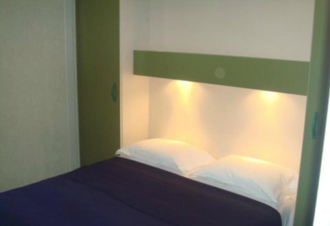 Knus tweepersoonsbed met groene accenten bij Bungalow Family, Wecamp Sao Miguel in Portugal, sfeerverlichting.