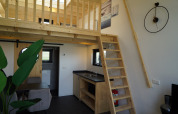 Interiør af Tiny House 2+2 i Hindeloopen, Holland, med hems, trætrappe, tekøkken og spiseområde.