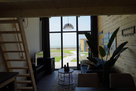 Interieur van Tiny House 2+2 in Hindeloopen, Nederland, met grote ramen en uitzicht op zee en tuinpad.