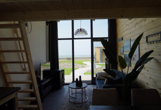 Interiør af Tiny House 2+2 i Hindeloopen, Nederlandene, med udsigt til terrasse og hav gennem store vinduer.