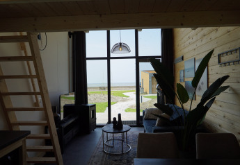 Interiør af Tiny House 2+2 i Hindeloopen, Nederlandene, med udsigt til terrasse og hav gennem store vinduer.