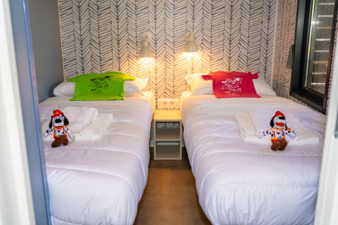 Dos camas individuales con camisetas coloridas, peluches de Goofy y luces modernas en Cottage Next XXL Prestige.