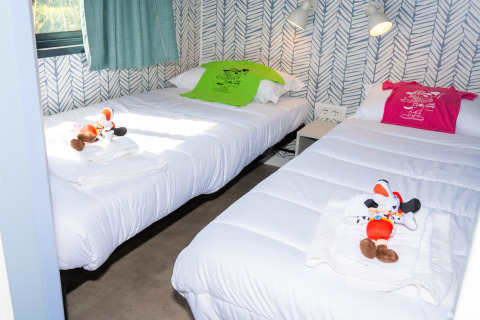 Dos camas individuales con temática de Mickey Mouse, peluches y camisetas de colores en una habitación luminosa.