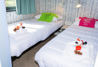 Dos camas individuales con temática de Mickey Mouse, peluches y camisetas de colores en una habitación luminosa.