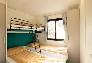 Camera da letto con letto a castello e due singoli nel Cottage Next XL Panorama al Trasimeno Glamping Resort, Italia.