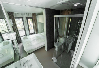 Camera da letto e bagno moderni con grandi finestre presso Cottage Next XL Panorama, Trasimeno Glamping Resort, Italia.