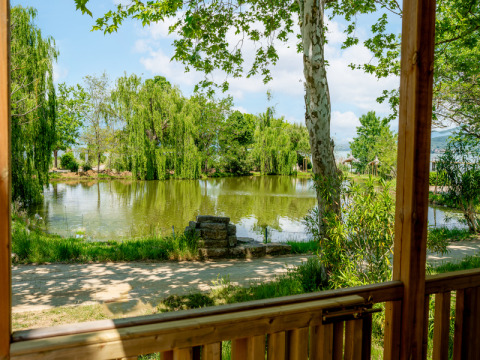 Vista desde la terraza del Cottage Next XL Loggia Laguna hacia un estanque y árboles en Trasimeno Glamping Resort, Italia.